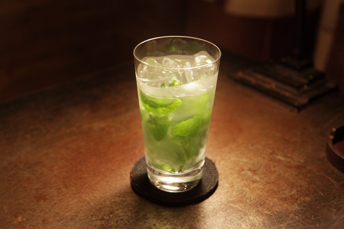 A mojito cocktail with fresh mint leaves and ice in a tall glass on a dark coaster.