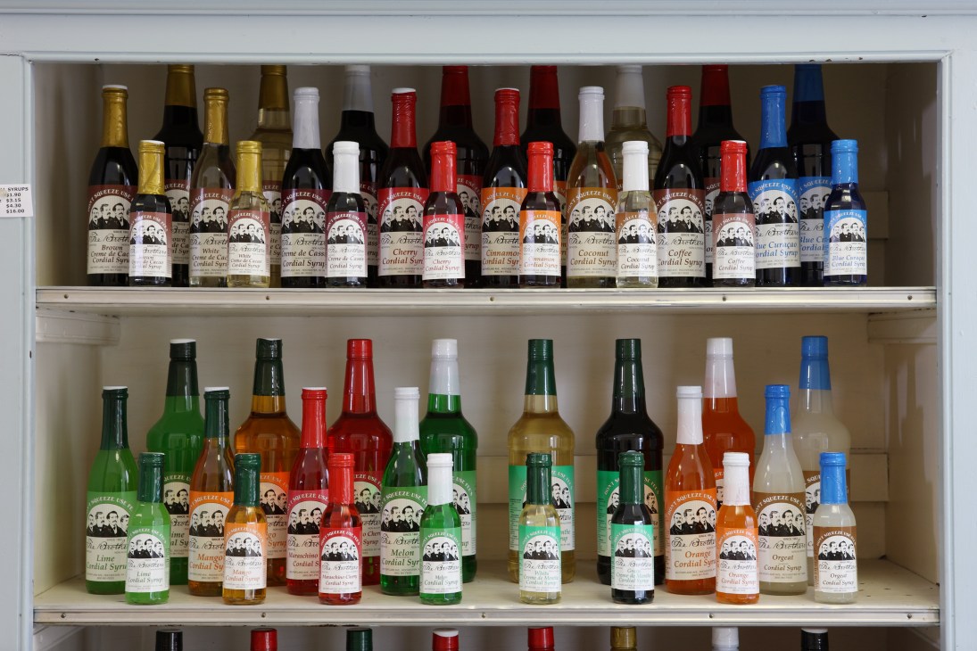 Display case showing Fee Brothers bitters bottles in various flavors with colorful caps arranged on two shelves.