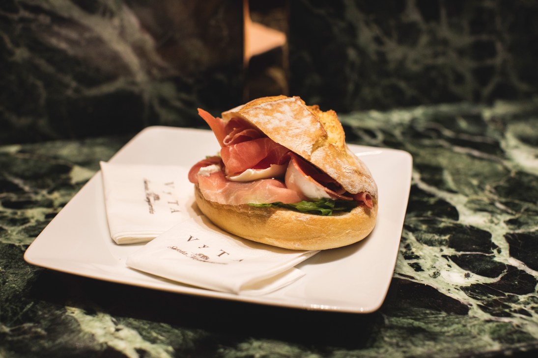 Gourmet sandwich with prosciutto and asparagus on white plate at Vyta bakery café.