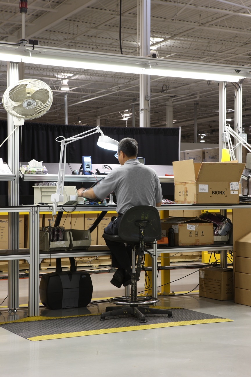 Worker assembling BionX electric bike system components at a factory workstation.