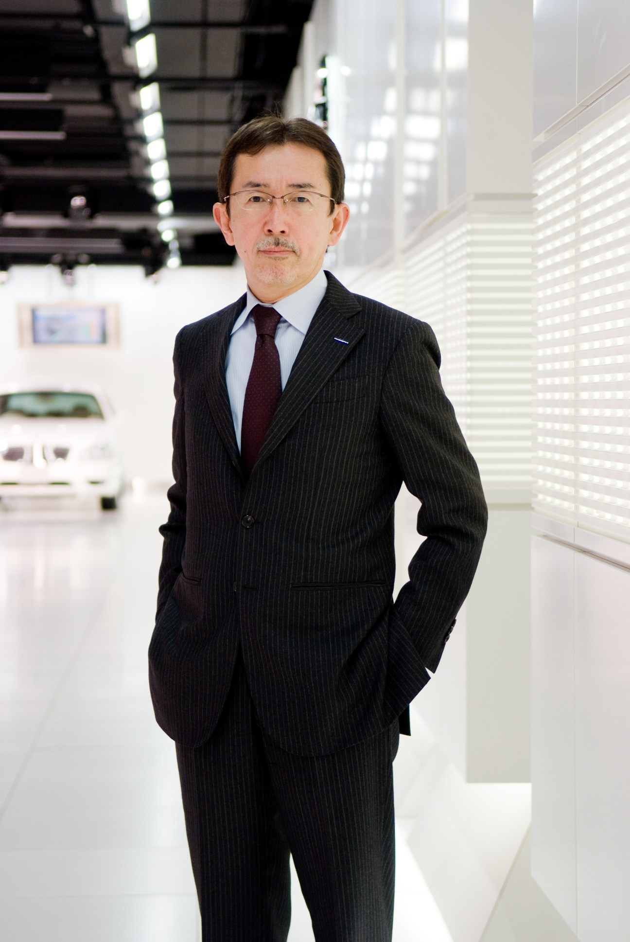 Shiro Nakamura, head of design at Nissan, standing in a modern showroom wearing a dark pinstriped suit.