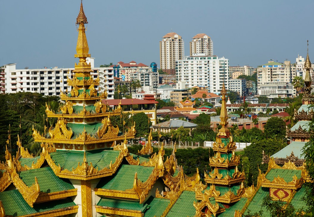 Golden-spired Buddhist temples with green roofs overlook modern apartment buildings in Yangon, Burma.