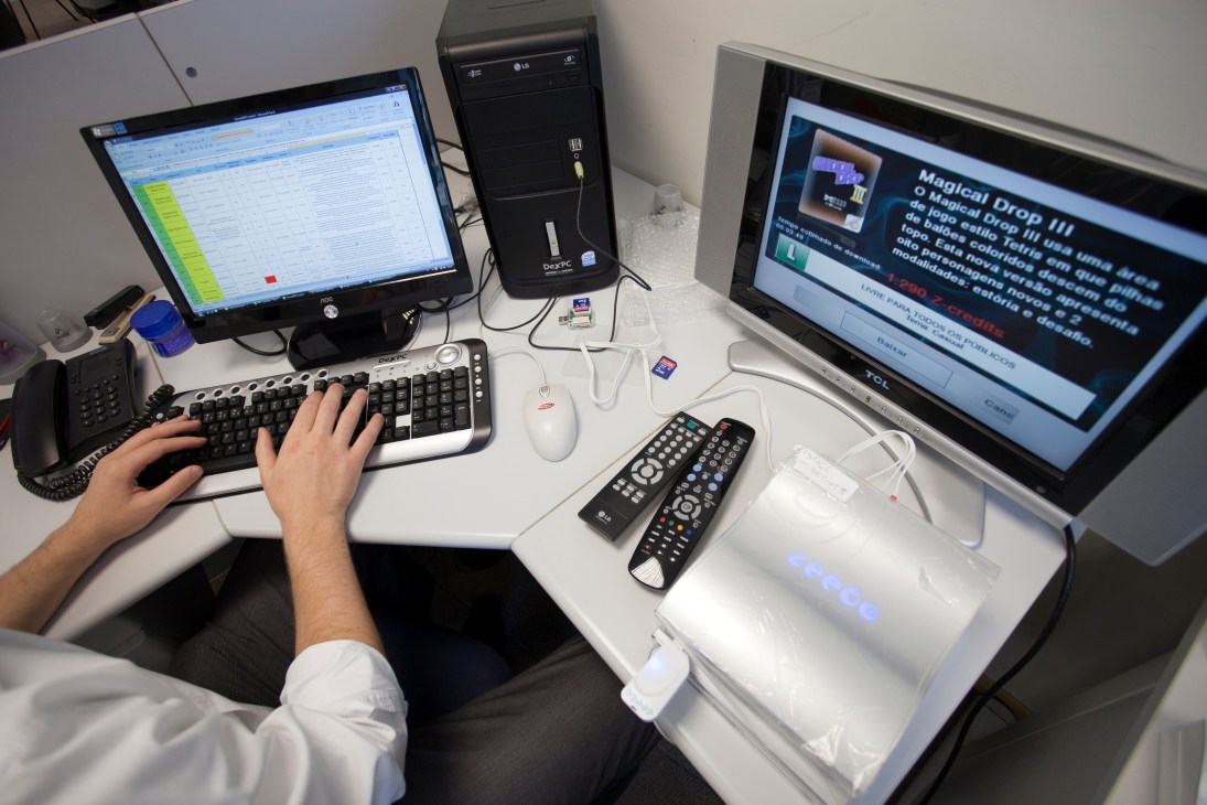 Person's hands typing at a keyboard while working at a computer desk with multiple monitors displaying software interfaces.