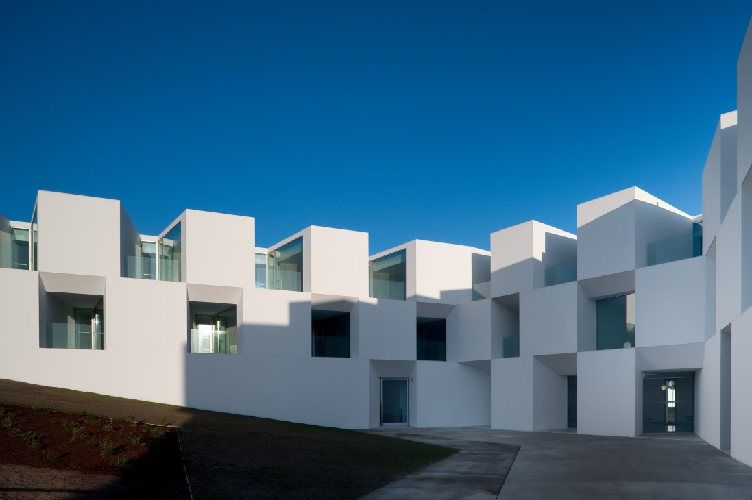 Modern white nursing home complex with angular geometric architecture and large windows under blue sky.