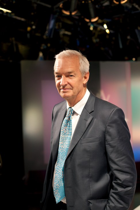 Jon Snow, principal newscaster at Channel 4 News, in a grey suit and patterned tie in a studio setting.