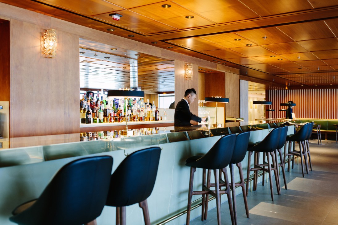 Cathay Pacific first-class lounge bar at Hong Kong Airport with blue chairs and illuminated shelving.