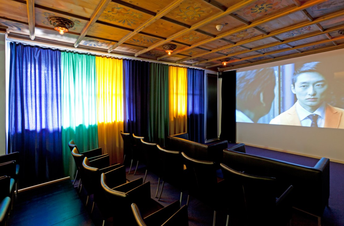 Private cinema screening room with colorful neon curtains, wooden coffered ceiling, and rows of black seats.