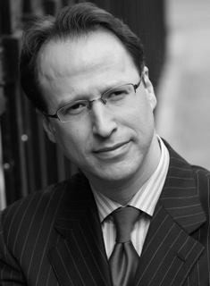 Black and white portrait of a man wearing glasses, pinstriped suit and tie.