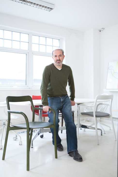 Man standing in bright office with modern chairs, including green and red designs.