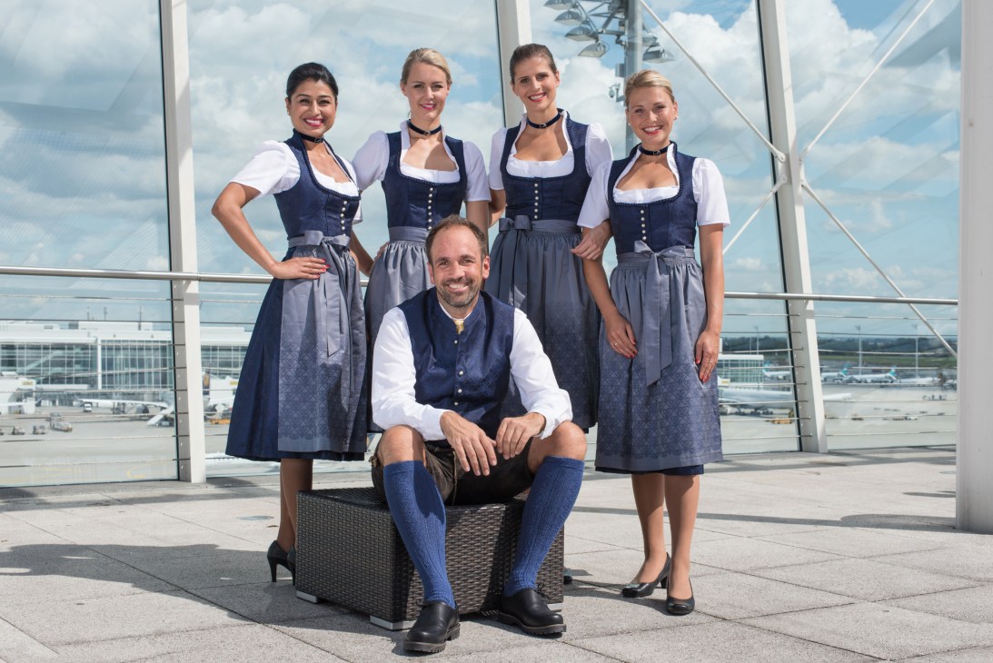 Lufthansa flight crew in traditional Bavarian dirndls and lederhosen uniforms with airport in background
