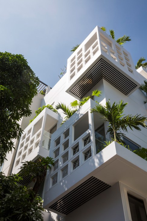 White modern residential building with balconies overflowing with green plants against a clear blue sky.