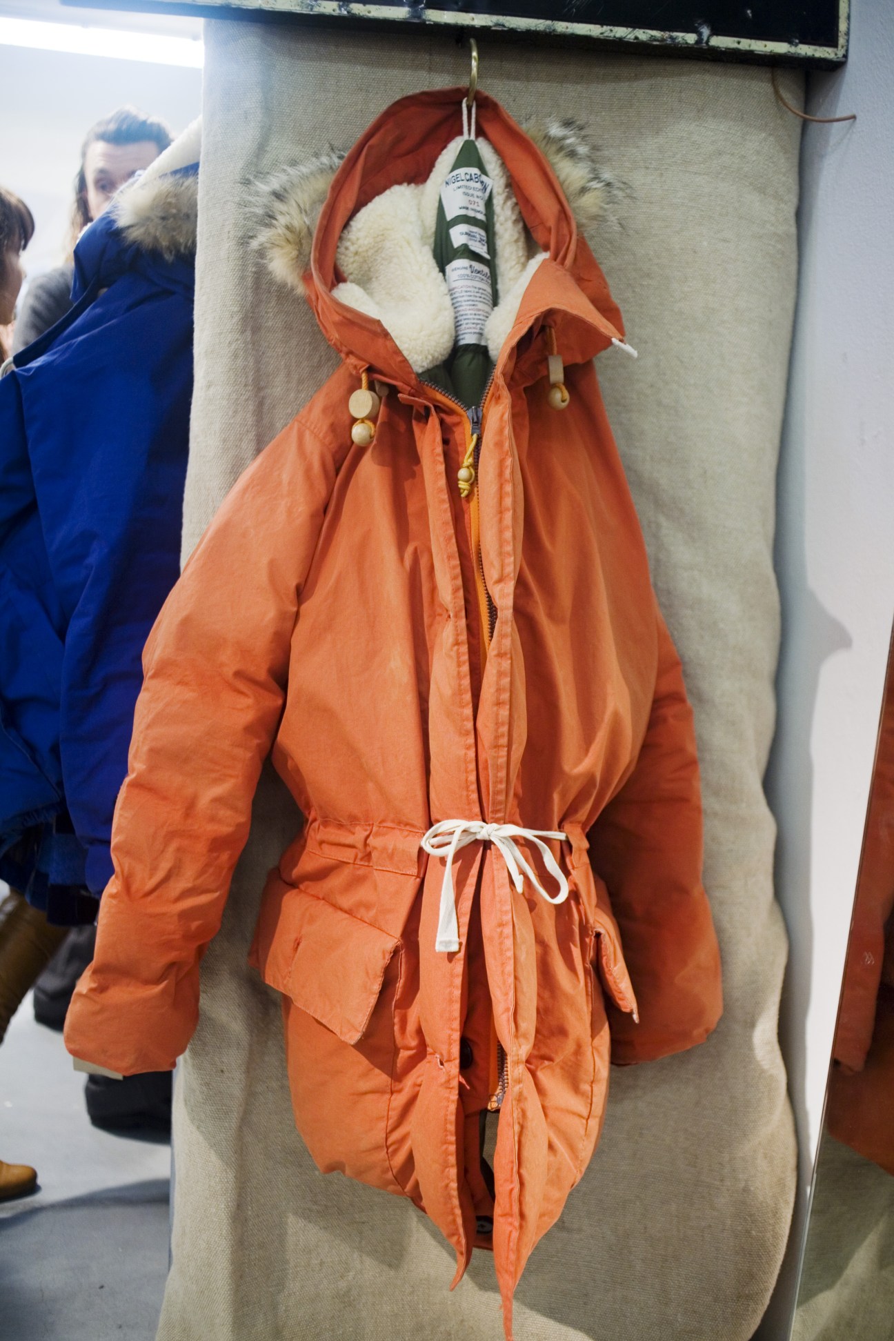 Orange down jacket with fur-lined hood and coyote trim displayed on a mannequin.