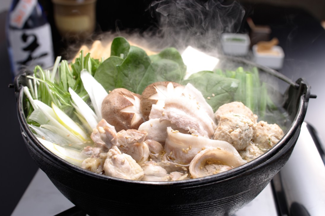 Steaming chanko nabe stew in a black pot with chicken, vegetables and broth.