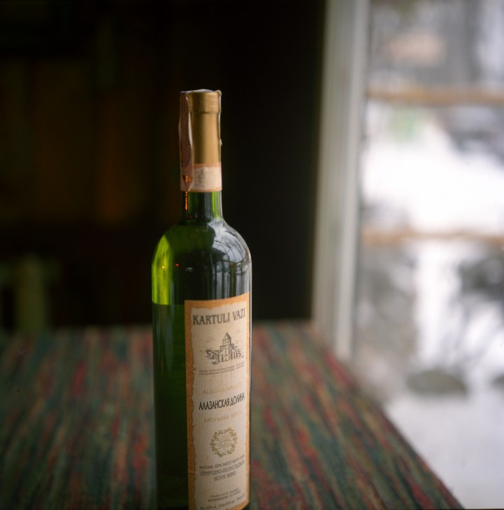 A bottle of Kartuli Vazi Georgian wine on a striped table with a blurred window in the background.