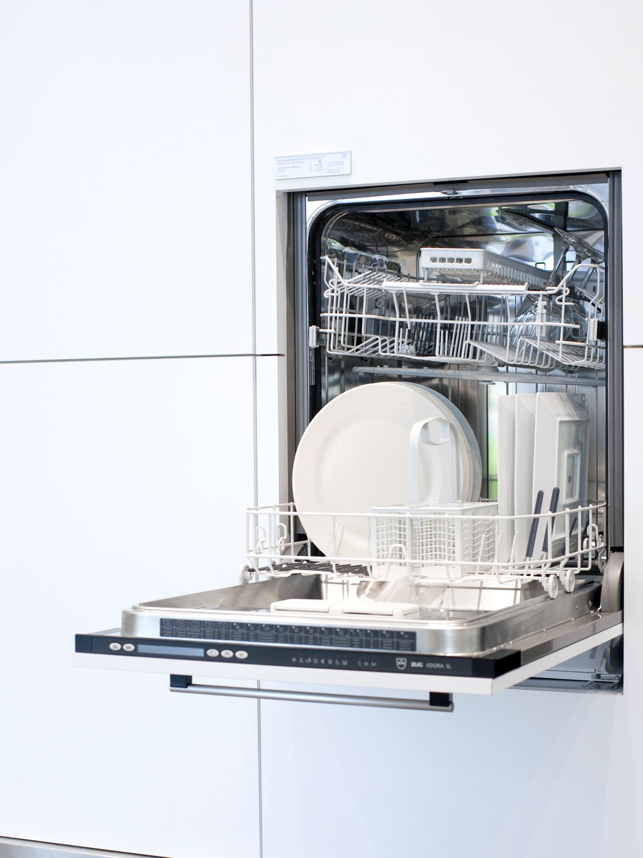 V-Zug dishwasher with open door displaying white plates and cutlery in racks.