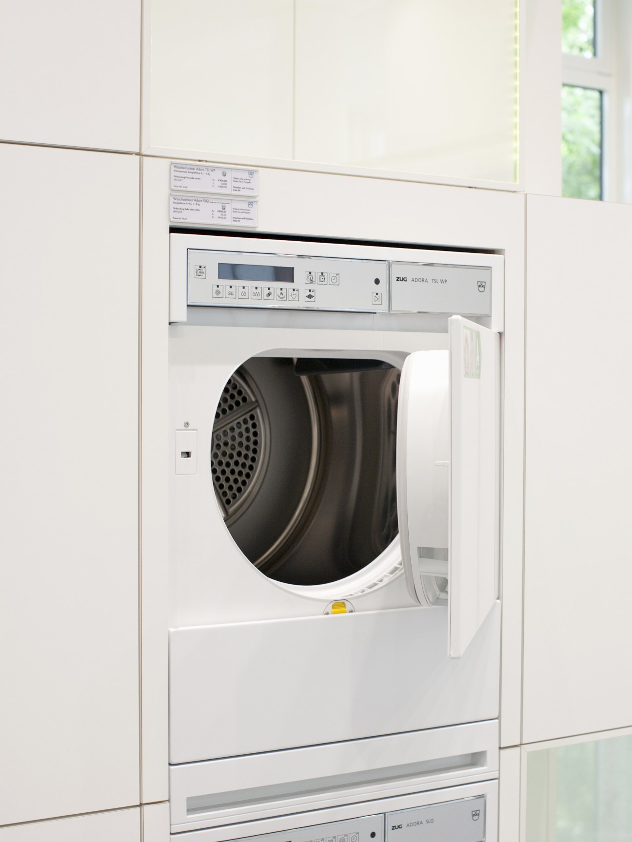 V-Zug heat-pump tumble dryer with white exterior and black drum displayed in showroom.