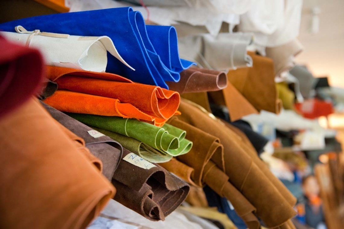 Rolled leather hides in various colors including blue, orange, white, brown, and green stacked together.