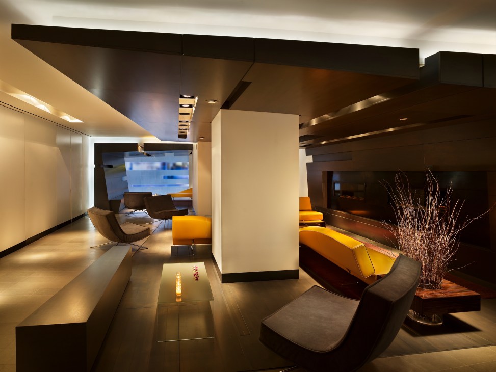 Modern hotel suite interior with orange seating, dark wood elements, and minimalist design featuring a lounge area with contemporary furnishings.