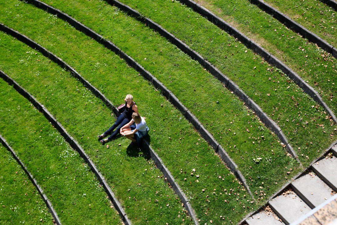 Aerial view of two people lying on moss-covered green sloped roof with dark beams.
