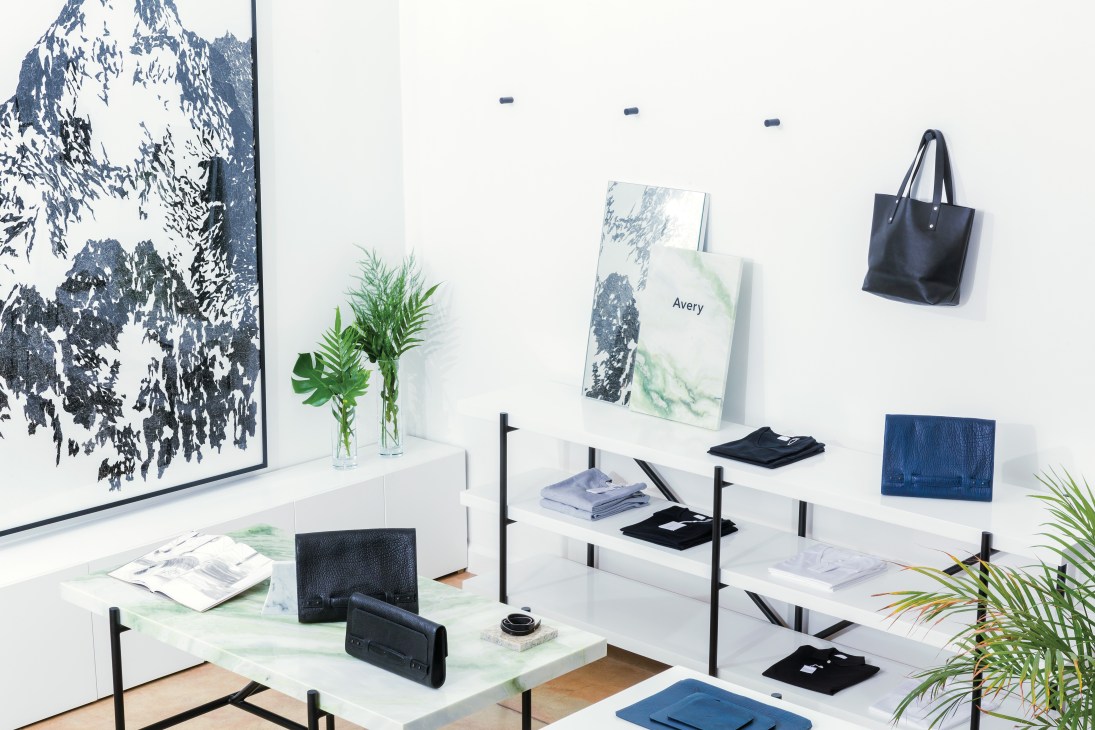 Avery boutique interior displaying fashion items including black wallets, bags and clothing on white shelving against a white wall.