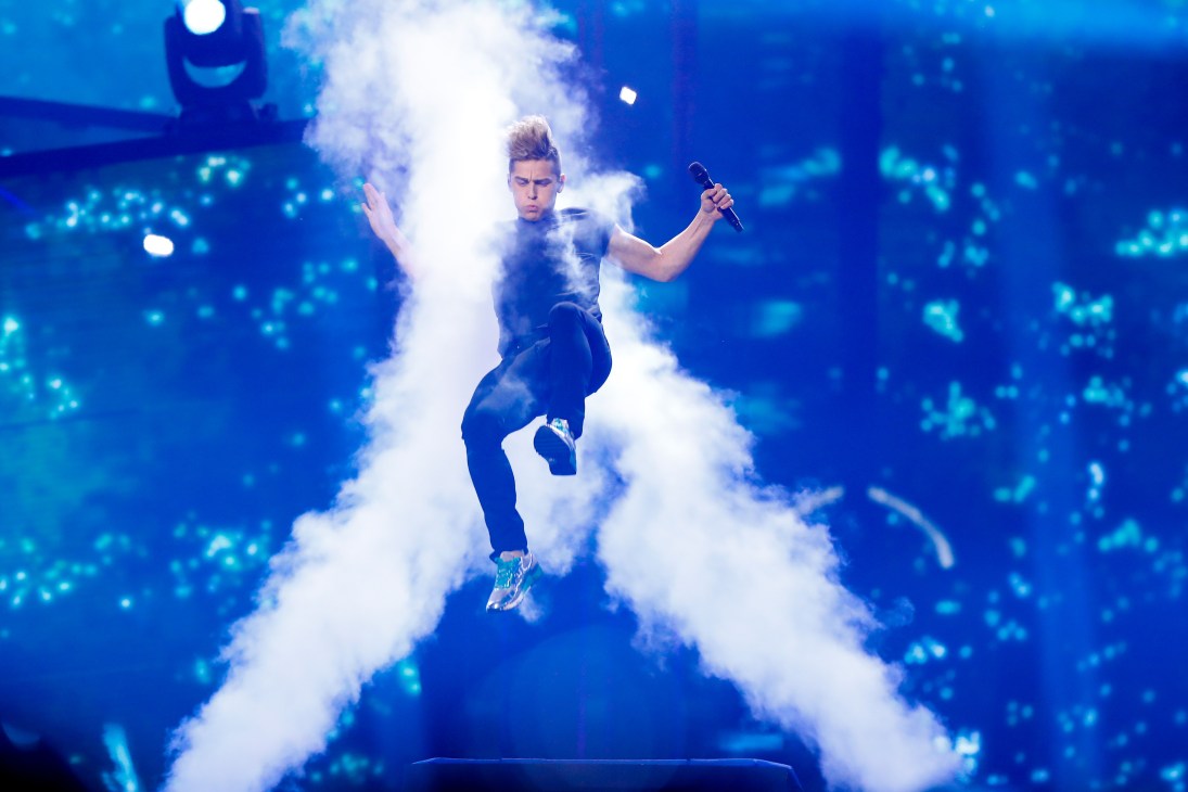 A performer sings on stage surrounded by dramatic white smoke and blue lighting effects.
