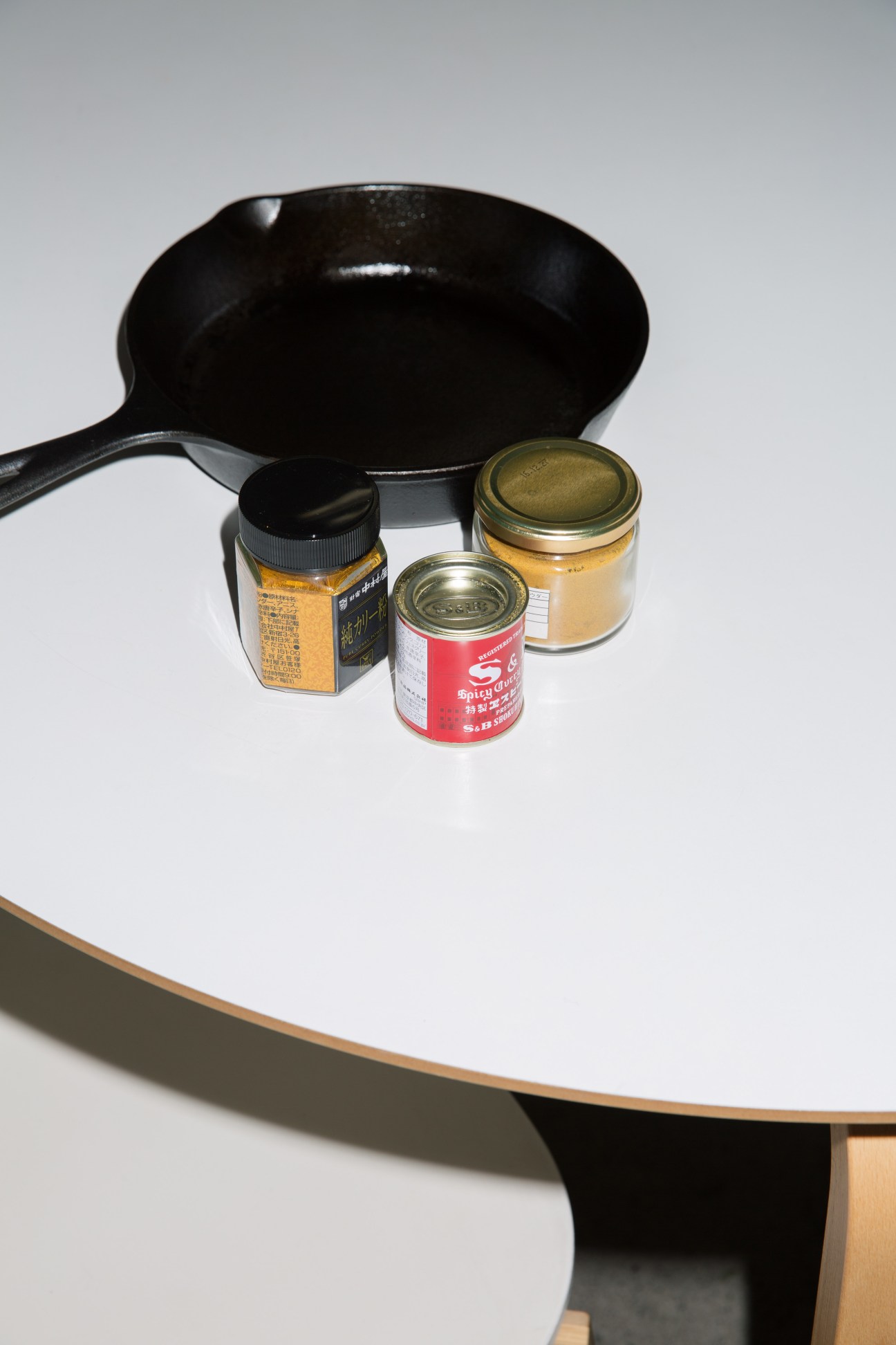 A black wok with cooking ingredients including jars of spices and paste on a wooden table.