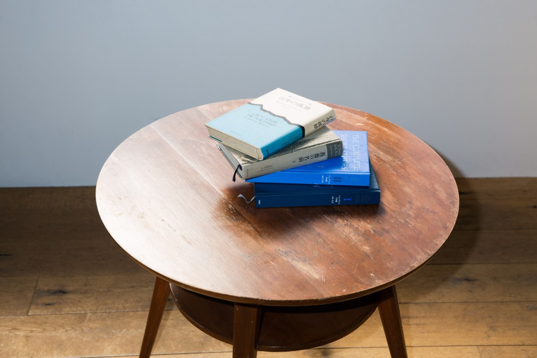 Stack of books on a round wooden table, including works by Gabriel García Márquez and Umberto Eco.