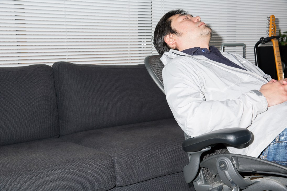 Man napping in an Aeron chair with head tilted back in an office setting.