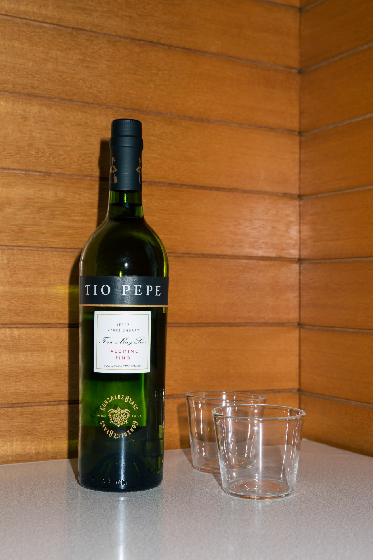 Bottle of Tío Pepe sherry with two empty glasses against a wooden wall backdrop.