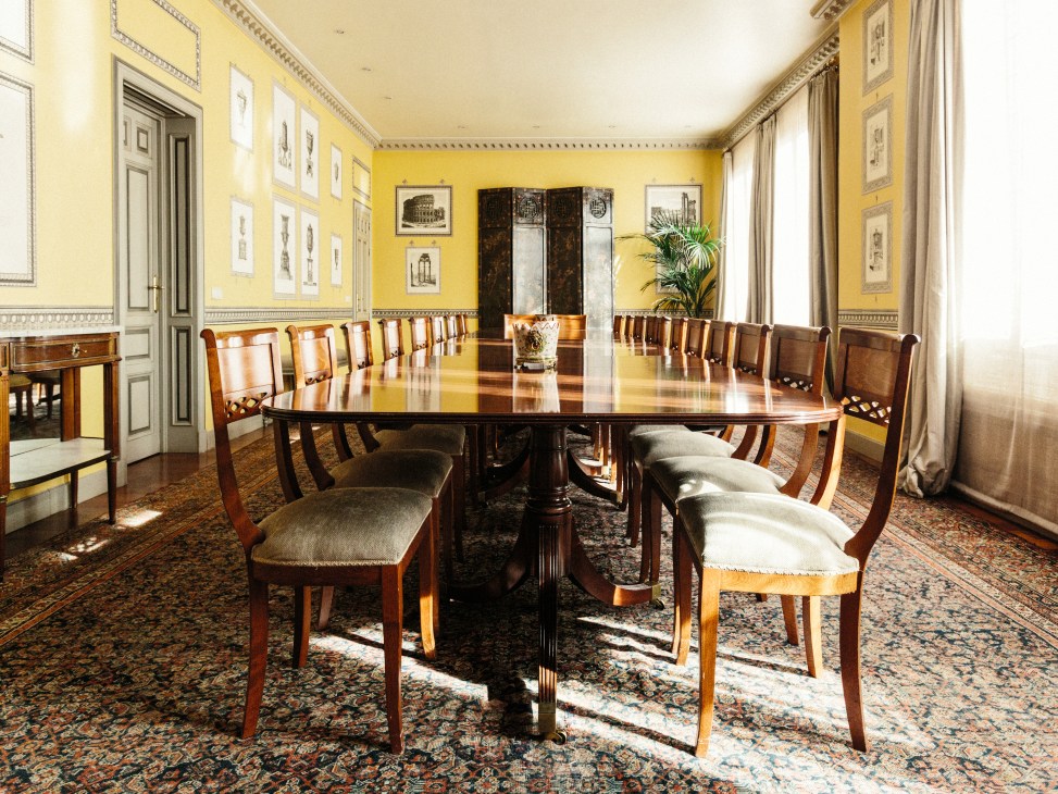 Elegant formal dining room with yellow walls, long wooden table and chairs at Real Instituto Elcano in Madrid.