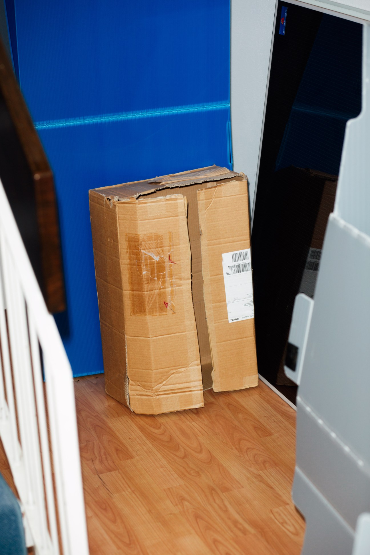 A worn cardboard box sitting on wooden flooring against a blue wall, symbolizing the moving industry waste that Turtlebox aims to reduce.