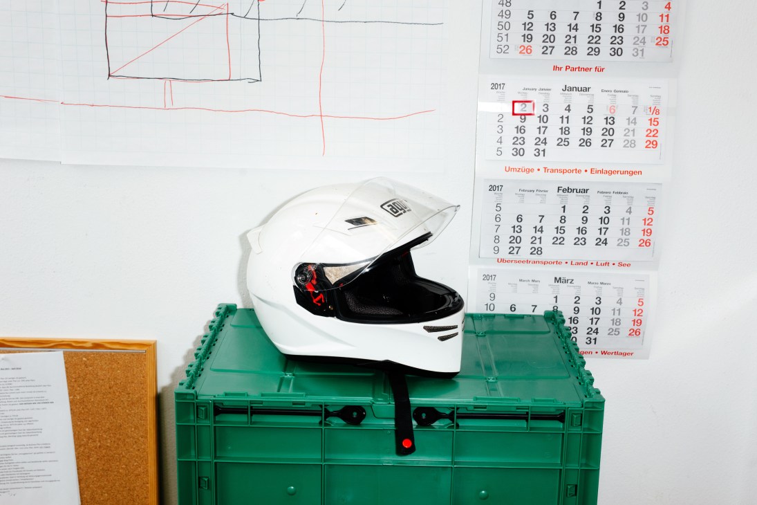 White motorcycle helmet with red accents placed on a green plastic storage crate next to calendars and sketches.