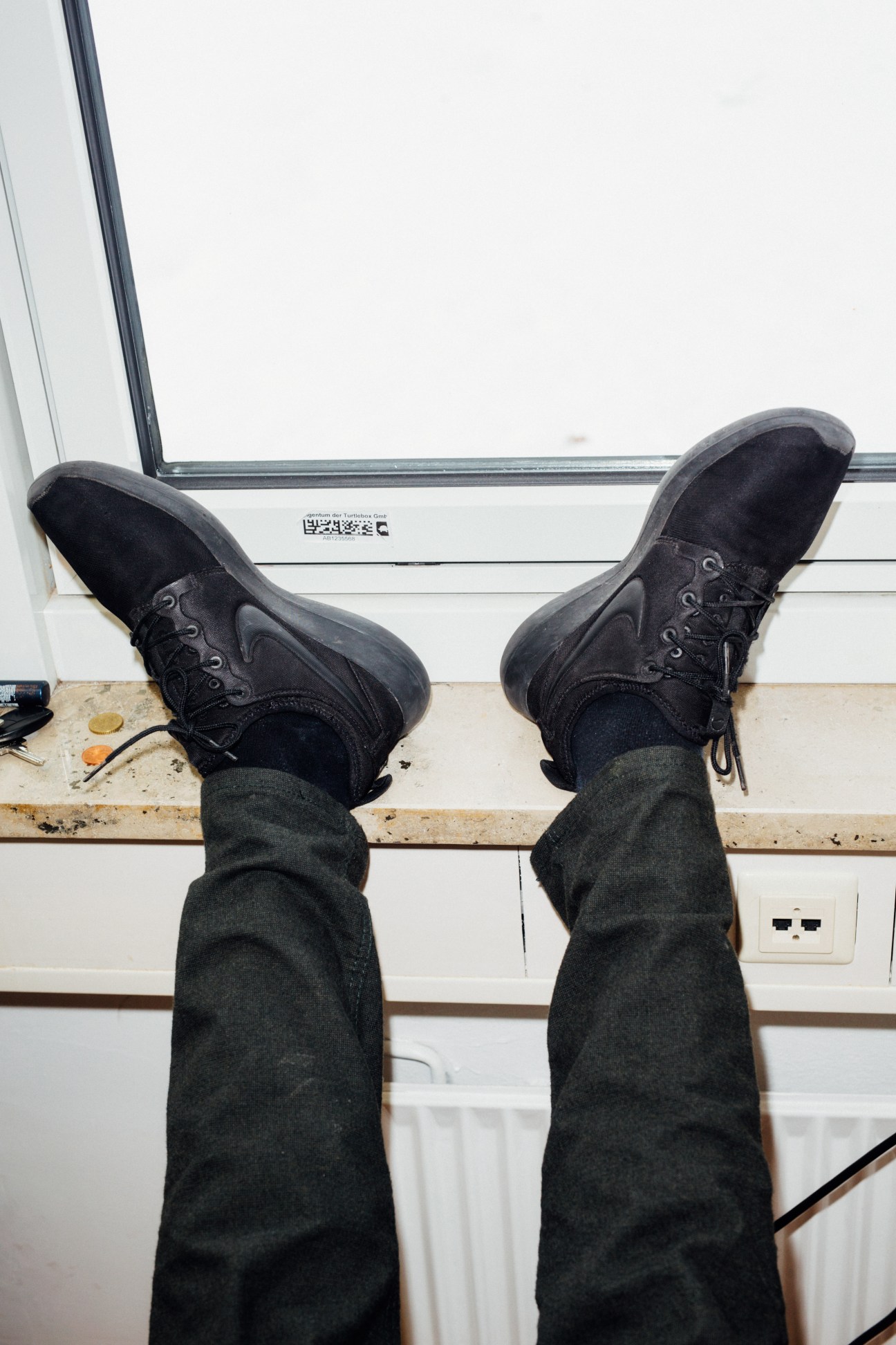 Person wearing black laced boots and dark trousers, feet up on a windowsill.
