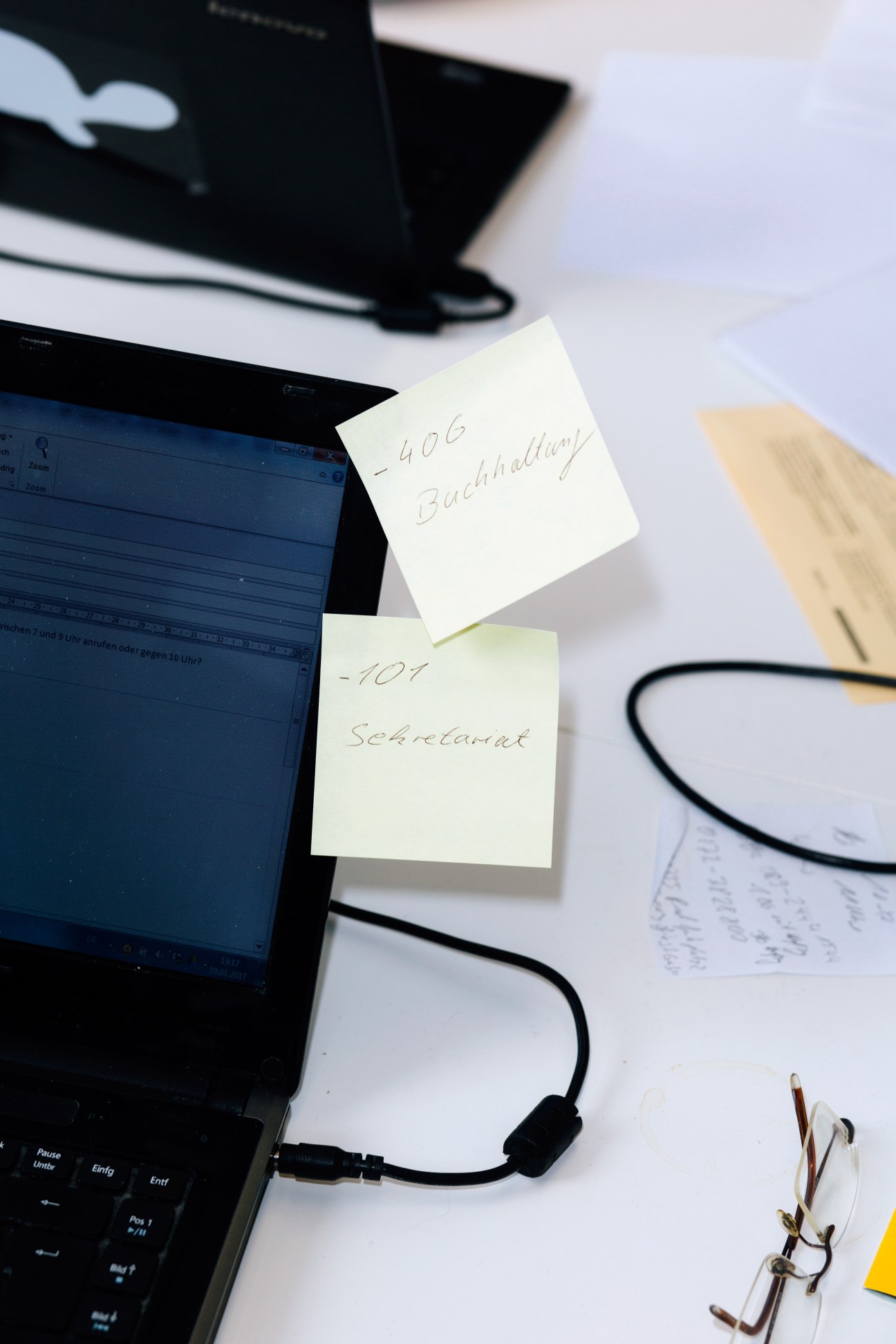 Laptop with handwritten sticky notes reading '406 Buchhaltung' and '101 Sekretariat' placed on its screen.