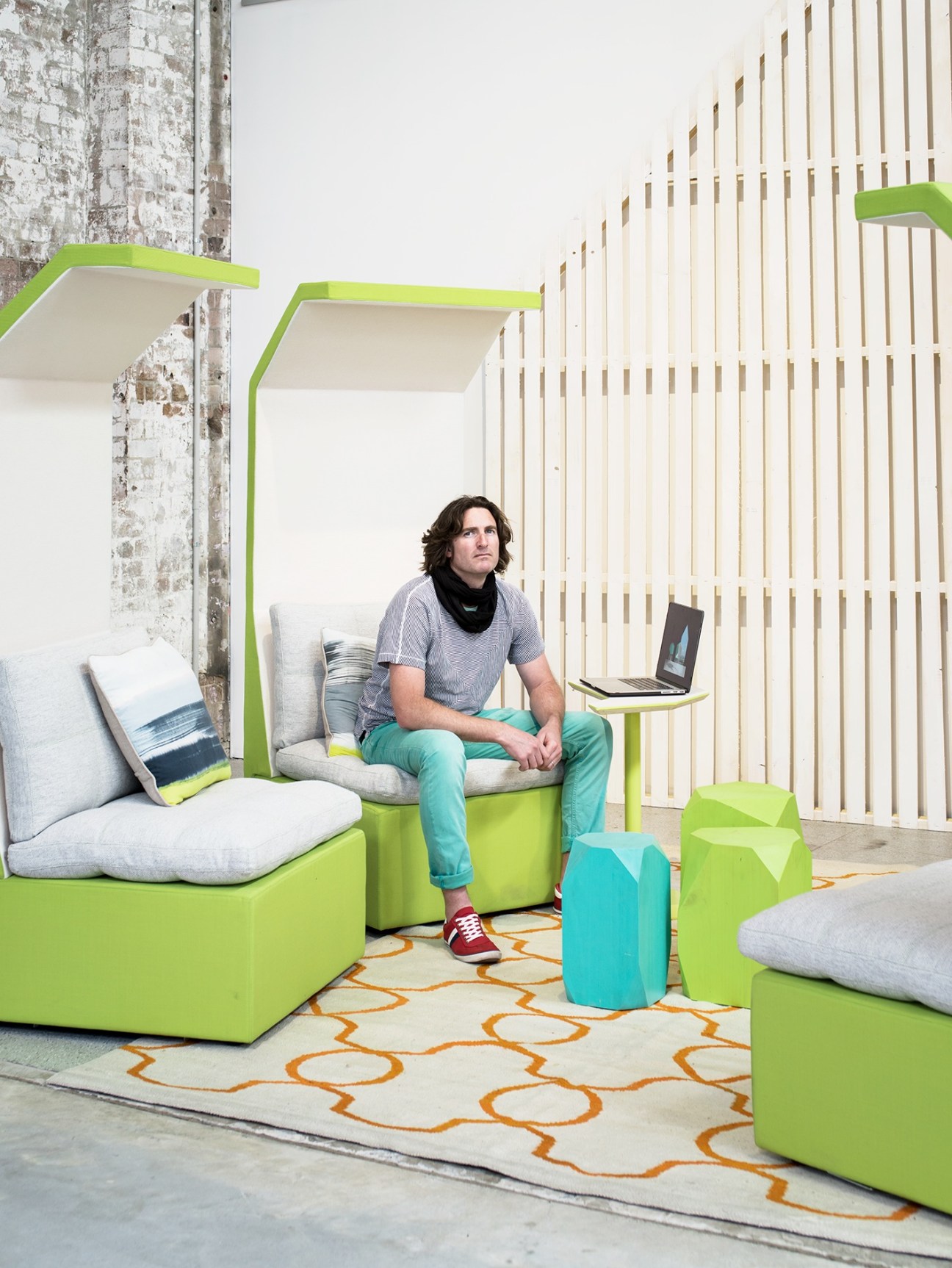 Man sitting in a bright green modular furniture pod with laptop in a modern office space.