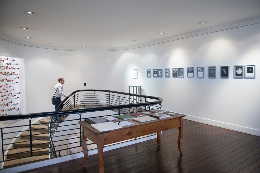 Gallery interior with curved staircase, wooden table, and framed artwork on white walls.