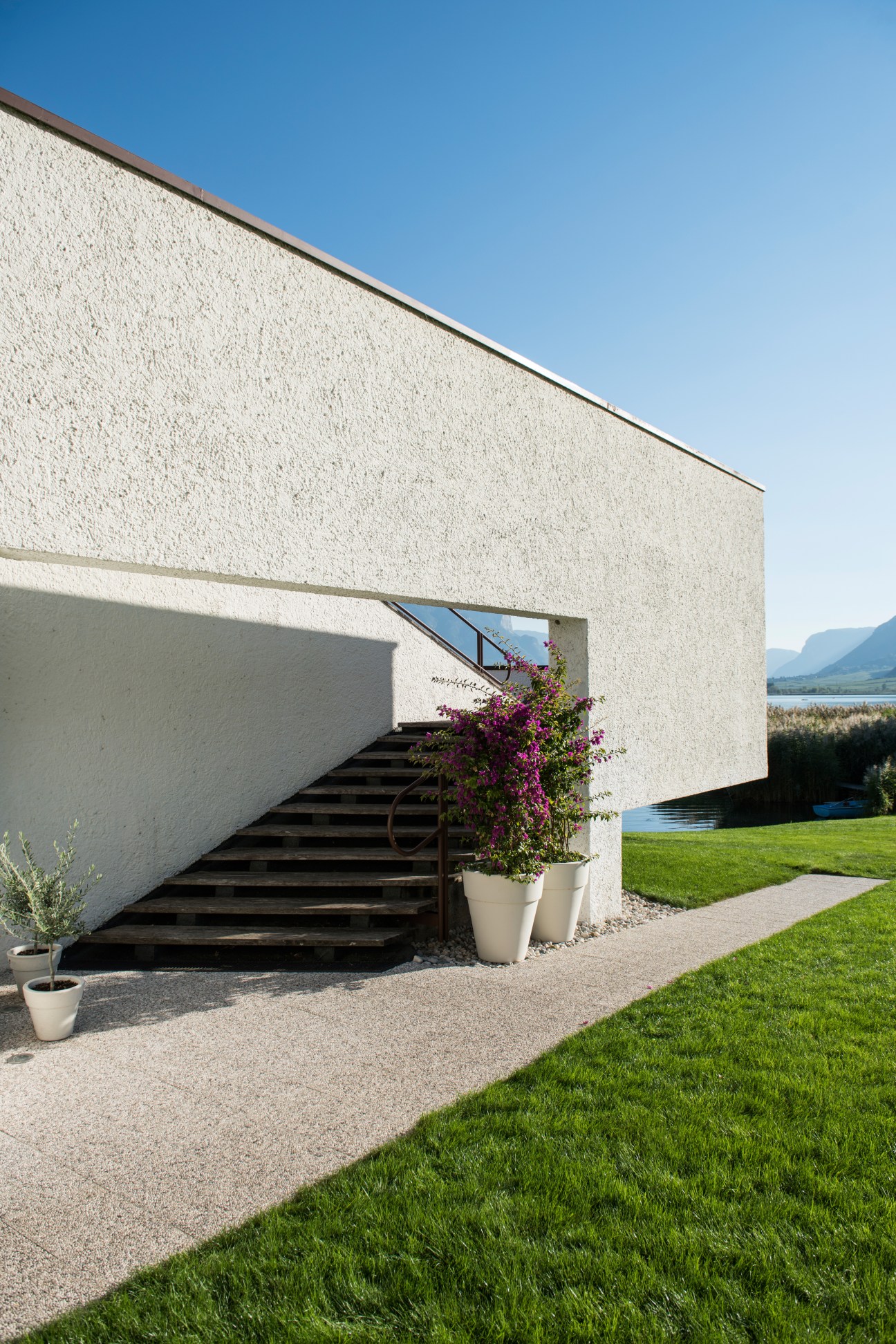 Modern white concrete lakeside pavilion with geometric balconies overlooking Lake Caldaro, Italy.