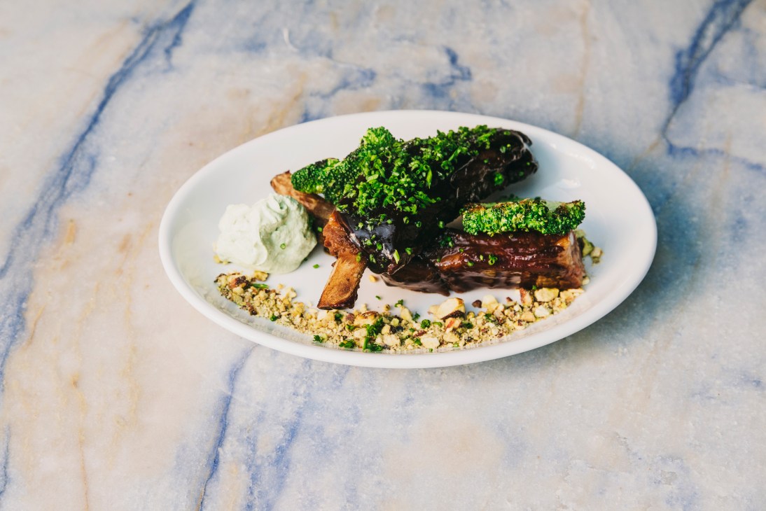 Plated dry-aged steak with charred broccoli florets topped with pistachio and chives, served with mustard cream and grain.