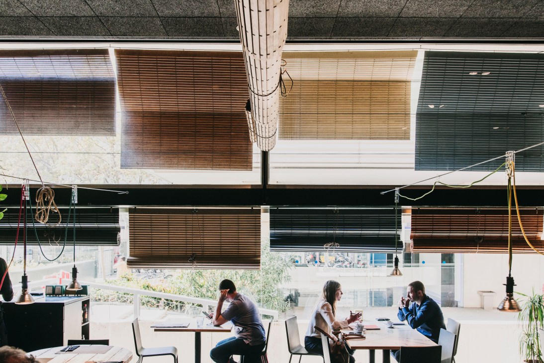 Modern cafe interior with wooden ceiling slats, pendant lights, and customers seated at tables