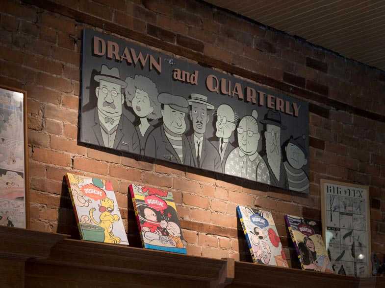 Drawn and Quarterly storefront with illuminated signage and graphic novels displayed on a wooden shelf against exposed brick.