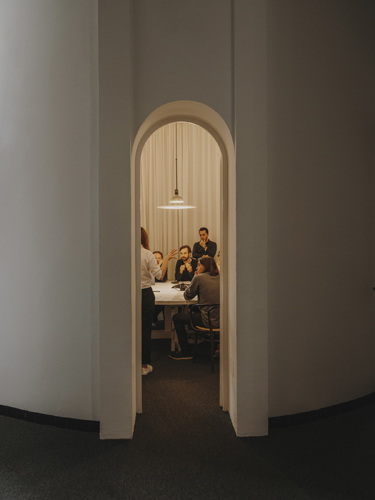 People in meeting pods inside an office with arched doorway and wooden interior structure.