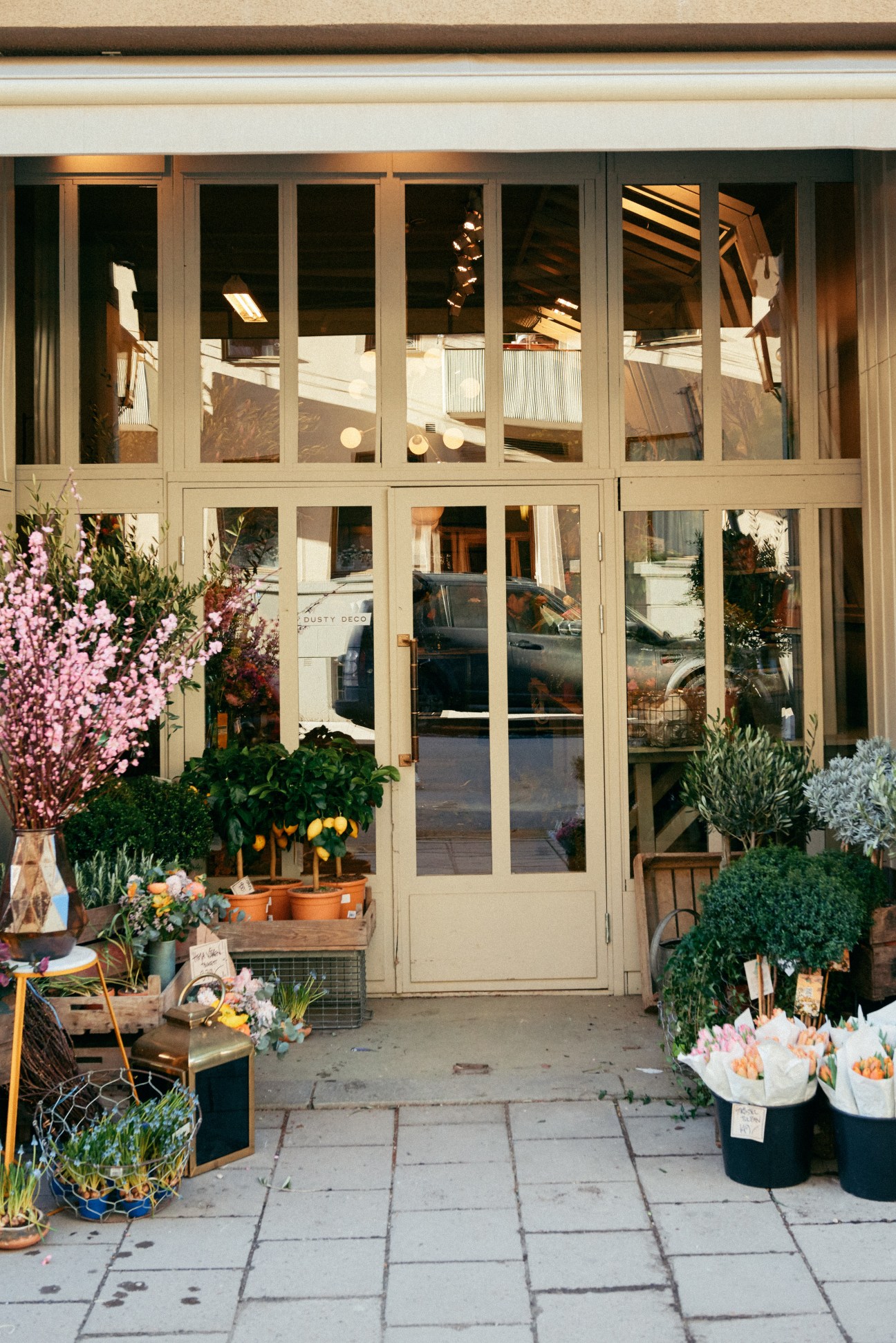 Dusty Deco vintage furniture shop storefront in Stockholm with cream-coloured doors and windows displaying plants and decorative objects.
