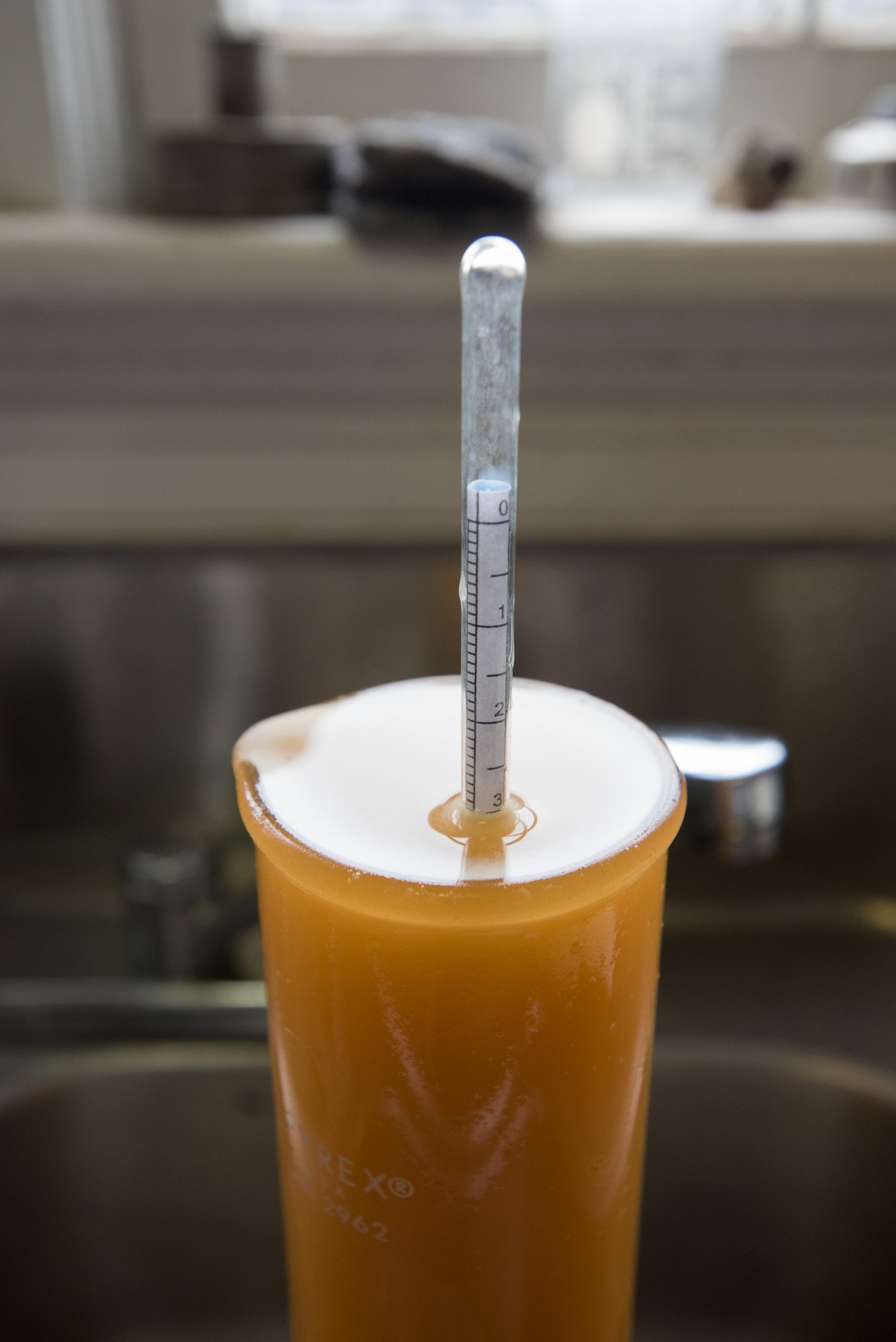 A vintage hydrometer measuring alcohol content in golden apple cider at Laird & Company distillery.