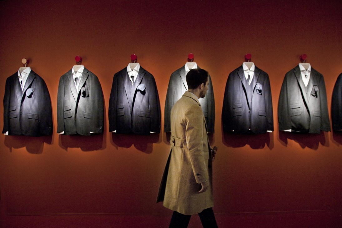A visitor examines pinstriped suits displayed on mannequins against an orange wall at Pitti Uomo.