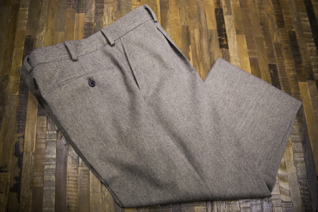 Pair of gray tailored trousers folded on a patterned wooden surface.