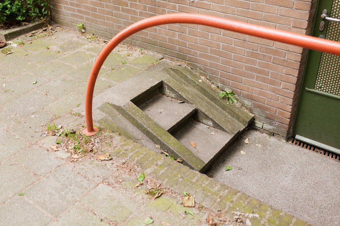 Orange metal ramp curved over brick steps for cyclists to push bikes up stairs in Amsterdam.