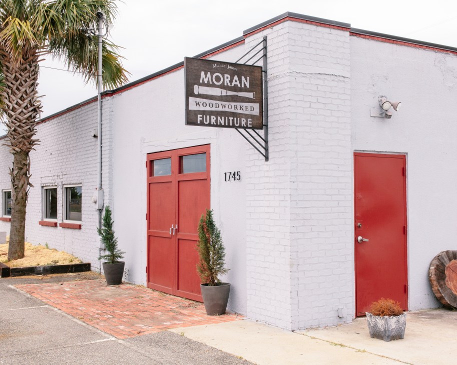 Michael James Moran Woodworked Furniture storefront with white brick, red doors and palm tree.