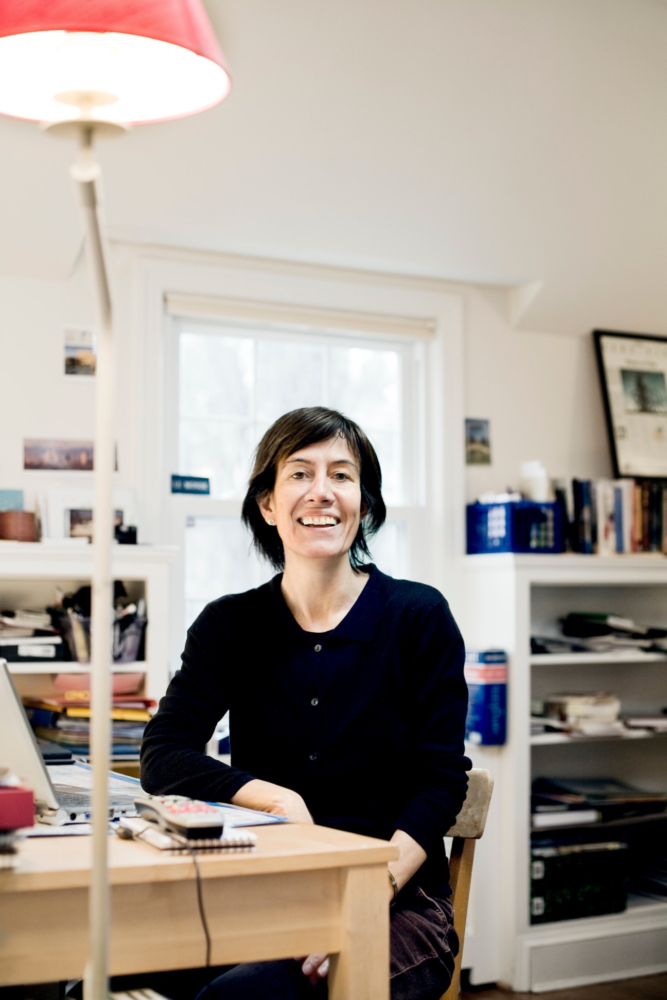 Woman sitting at desk in bright office with shelving and red pendant lamp
