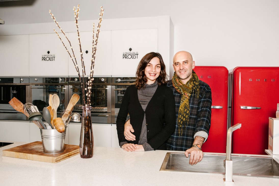 Laura Martínez and Néstor Calvo stand in their organic supermarket kitchen with red SMEG refrigerators and kitchen tools.