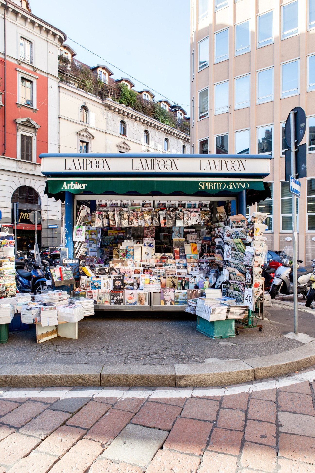 Italian newsagent kiosk with blue and white storefront displaying newspapers, magazines and publications.